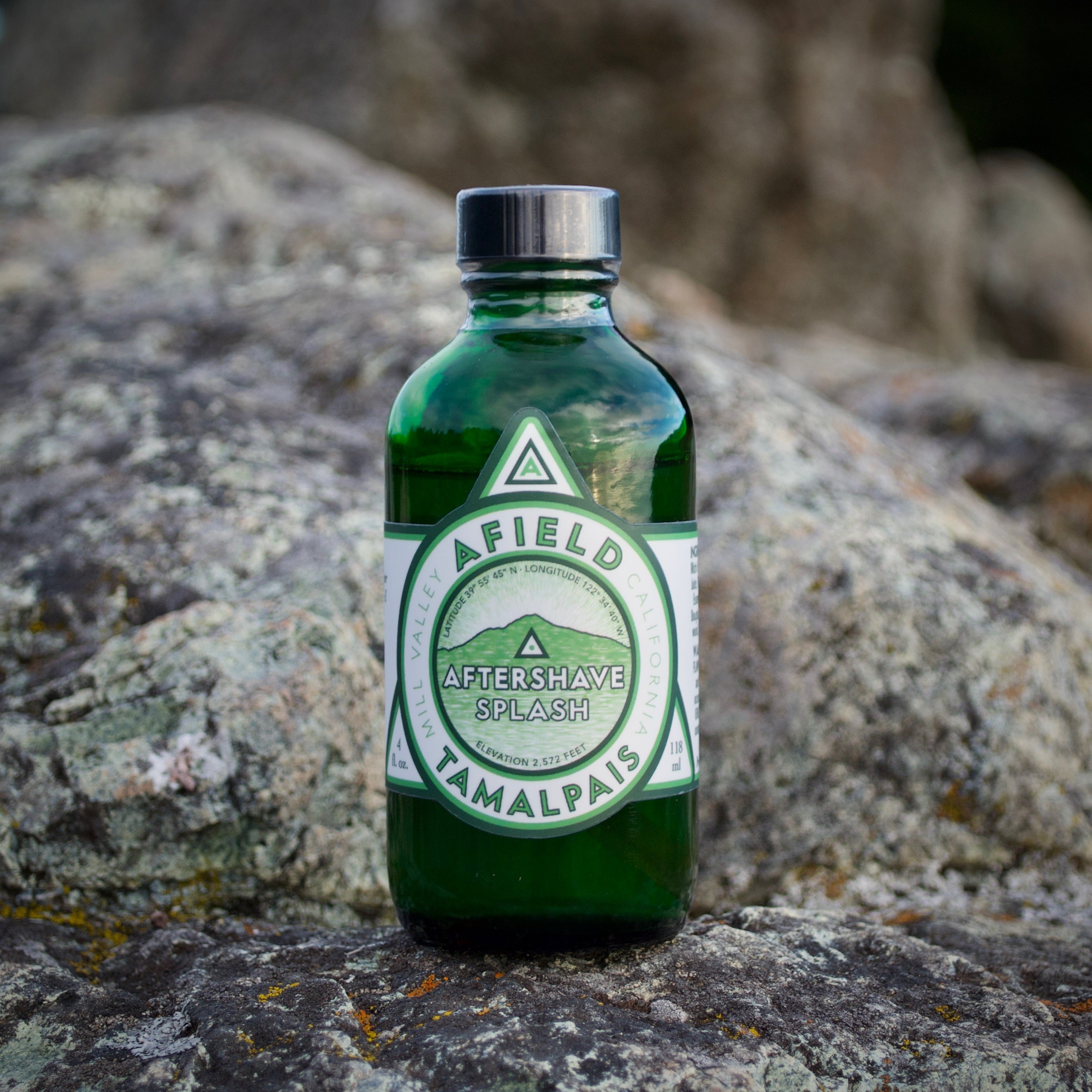 Green glass Afield Tamalpais Aftershave Splash bottle with a label on a rock with a natural background.