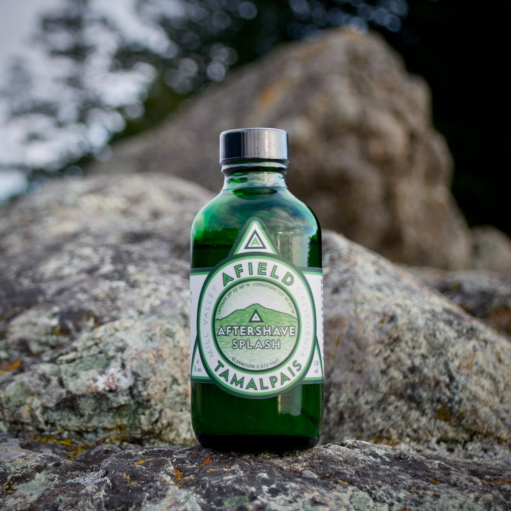 Green glass Afield Tamalpais Aftershave Splash bottle with a label on a rock with a natural background.
