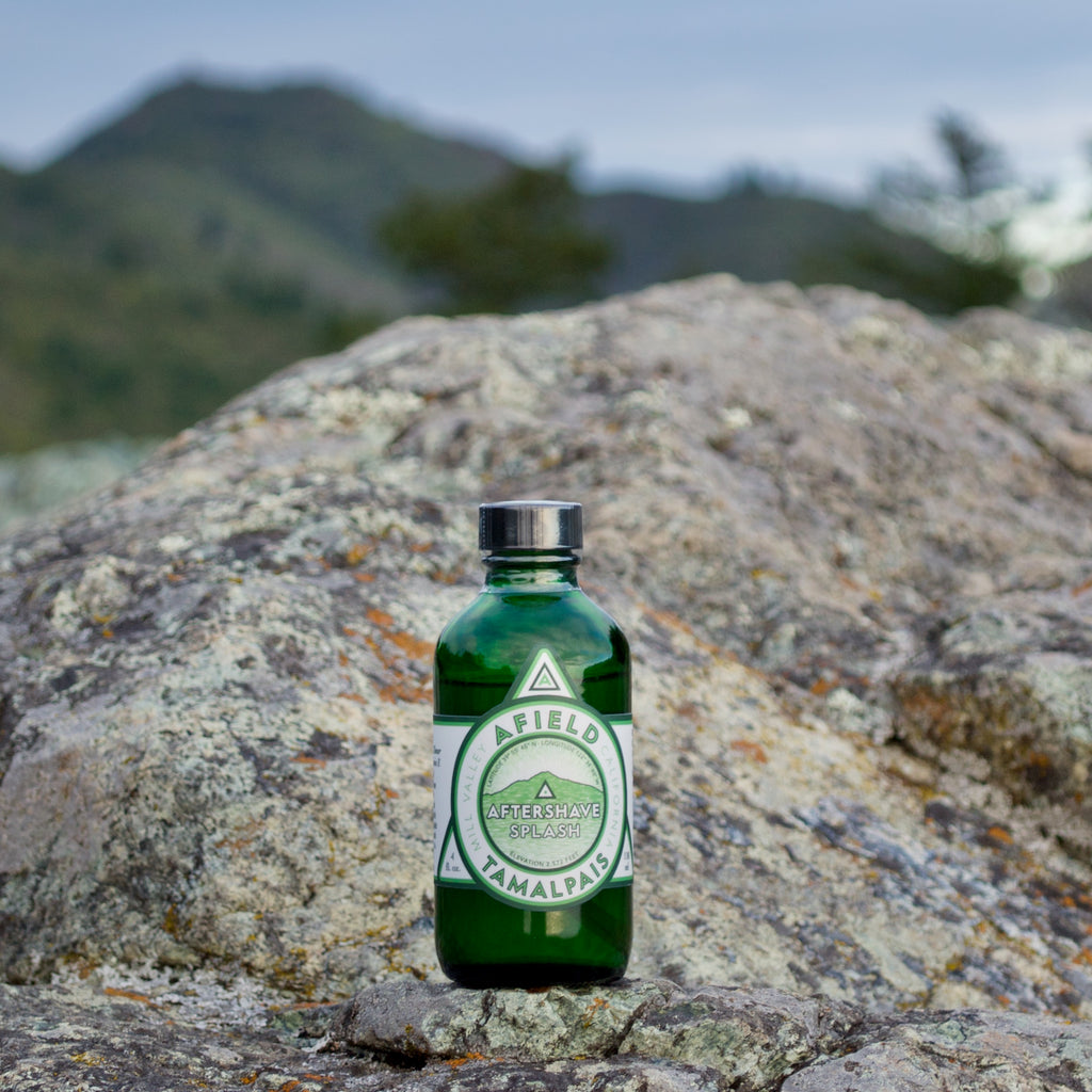 Green glass Afield Tamalpais Aftershave Splash bottle with a label on a rock with Mount Tamalpais in the background.