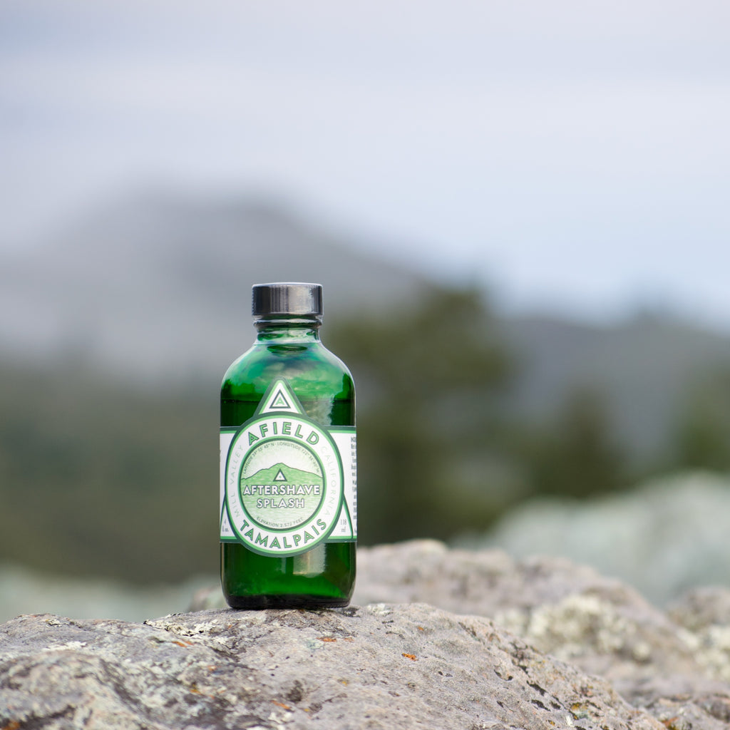 Green glass Afield Tamalpais Aftershave Splash bottle with a white label on a rock with foggy Mount Tamalpais in the background.