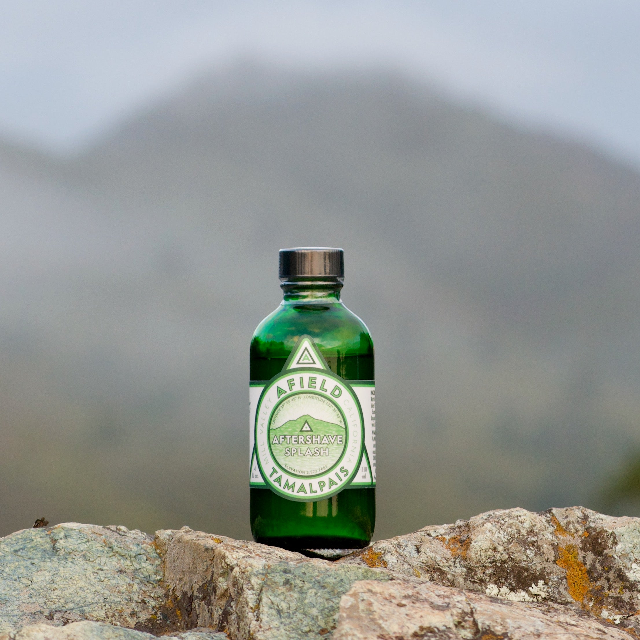 Green glass Afield Tamalpais Aftershave Splash bottle with a white label on a rock with Mount Tamalpais in the background.